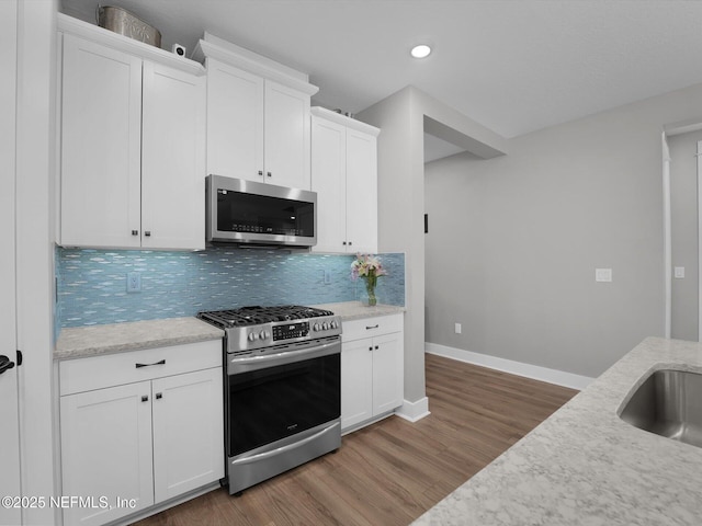 kitchen with hardwood / wood-style floors, white cabinets, stainless steel appliances, and tasteful backsplash