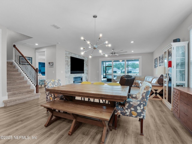 dining space featuring light wood-type flooring, a premium fireplace, and ceiling fan with notable chandelier