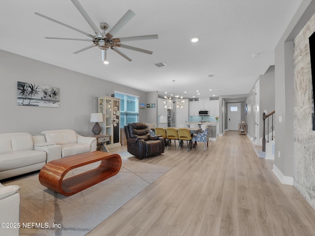 living room featuring light wood-type flooring and ceiling fan with notable chandelier