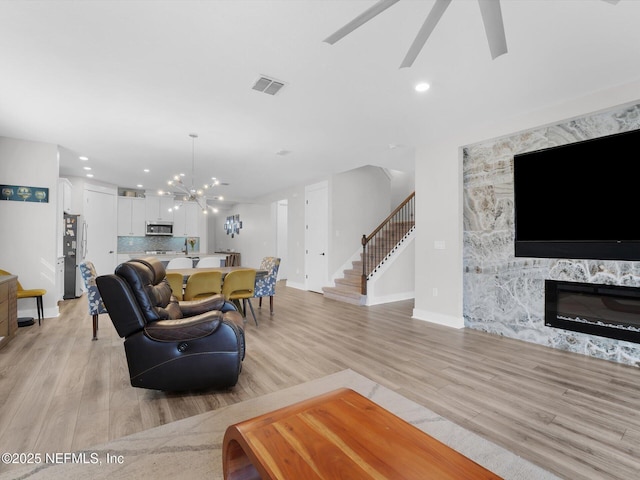 living room featuring ceiling fan with notable chandelier and light wood-type flooring