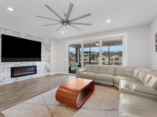 living room featuring ceiling fan, a healthy amount of sunlight, a premium fireplace, and light wood-type flooring