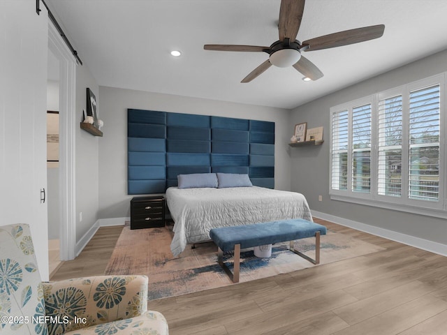 bedroom with ceiling fan, a barn door, and light wood-type flooring