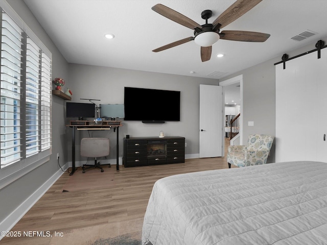 bedroom featuring ceiling fan, a barn door, and light hardwood / wood-style flooring