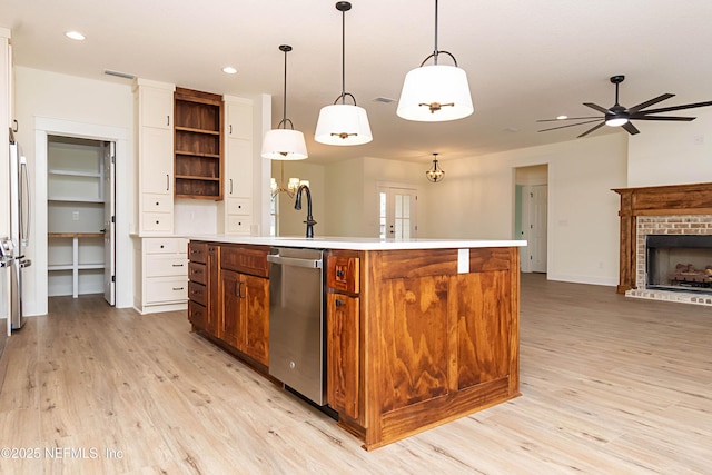 kitchen featuring a center island with sink, a brick fireplace, ceiling fan, hanging light fixtures, and stainless steel dishwasher