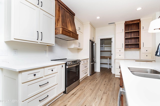 kitchen with appliances with stainless steel finishes, light hardwood / wood-style floors, white cabinets, and custom range hood