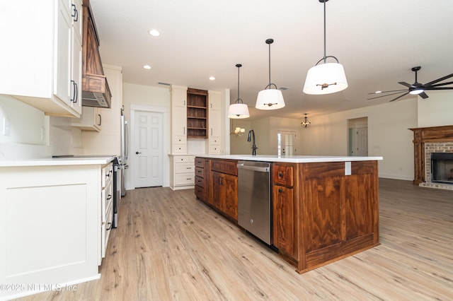 kitchen featuring a brick fireplace, appliances with stainless steel finishes, ceiling fan, a kitchen island with sink, and pendant lighting