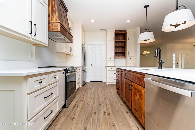 kitchen with appliances with stainless steel finishes, white cabinets, pendant lighting, light hardwood / wood-style flooring, and sink