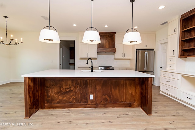 kitchen featuring premium range hood, stainless steel appliances, decorative light fixtures, a large island with sink, and sink