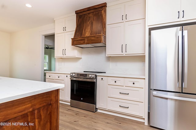 kitchen with stainless steel appliances, custom range hood, white cabinets, light stone countertops, and light hardwood / wood-style flooring