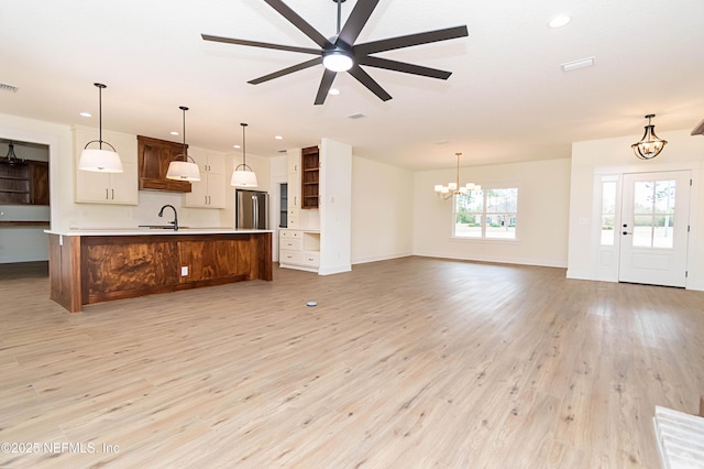 kitchen with decorative light fixtures, light hardwood / wood-style floors, stainless steel refrigerator, a large island, and ceiling fan with notable chandelier