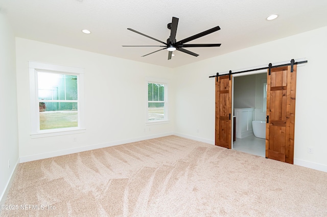 carpeted spare room with ceiling fan and a barn door