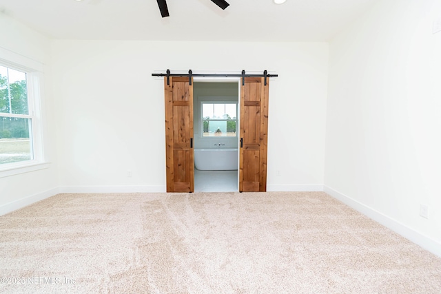 unfurnished room featuring ceiling fan, carpet flooring, and a barn door