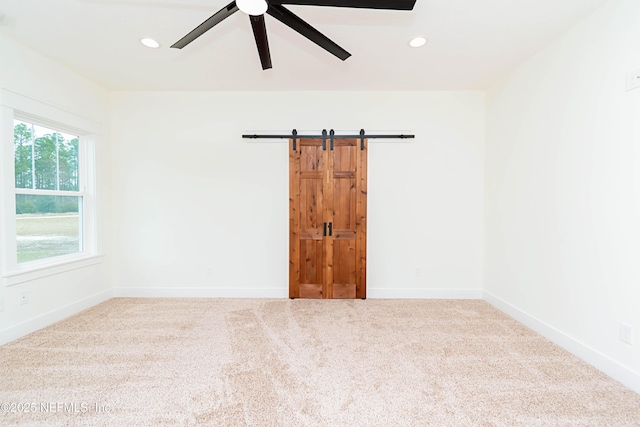 carpeted empty room featuring ceiling fan and a barn door