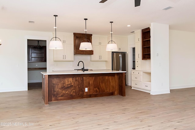 kitchen featuring decorative light fixtures, ceiling fan, sink, light wood-type flooring, and an island with sink