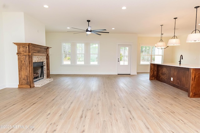 unfurnished living room with ceiling fan, a fireplace, light hardwood / wood-style flooring, and sink