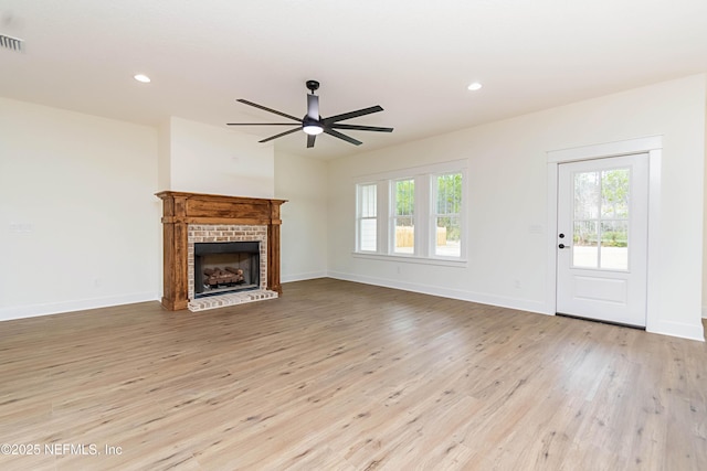 unfurnished living room with light wood-type flooring, a brick fireplace, and ceiling fan