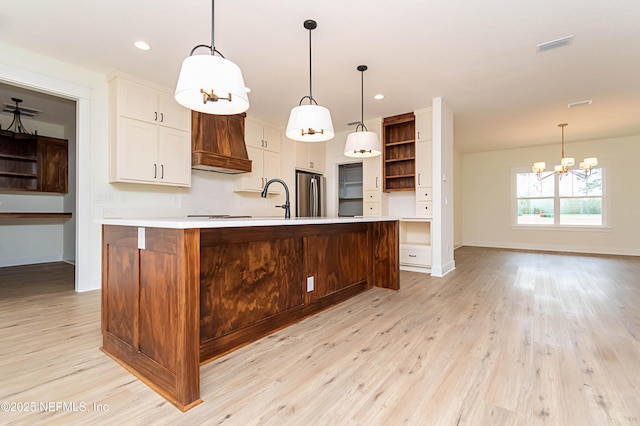 kitchen featuring a large island with sink, premium range hood, stainless steel fridge, a chandelier, and light hardwood / wood-style flooring