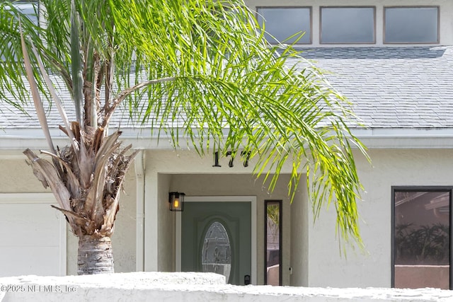 property entrance with a garage, roof with shingles, and stucco siding