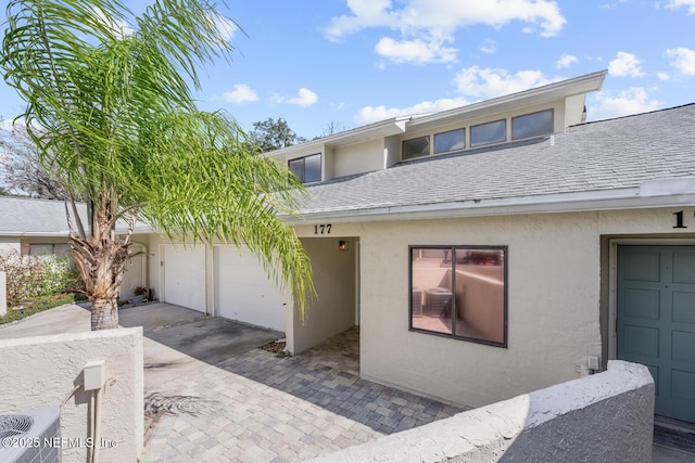 townhome / multi-family property with stucco siding, central air condition unit, driveway, roof with shingles, and an attached garage