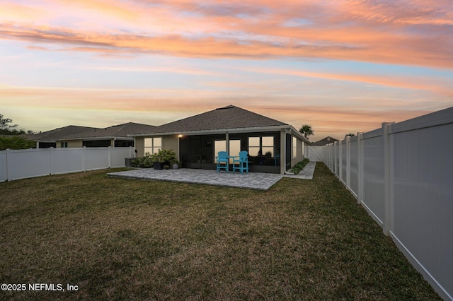 back house at dusk featuring a patio area and a lawn