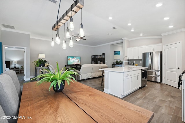 kitchen featuring stainless steel appliances, sink, white cabinetry, hanging light fixtures, and a center island with sink