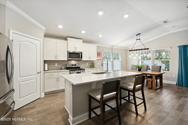 kitchen featuring stainless steel appliances, sink, white cabinets, vaulted ceiling, and an island with sink