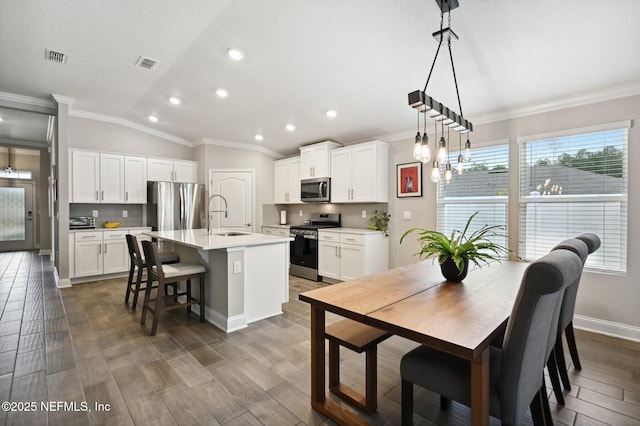 kitchen featuring stainless steel appliances, an island with sink, sink, white cabinetry, and decorative light fixtures