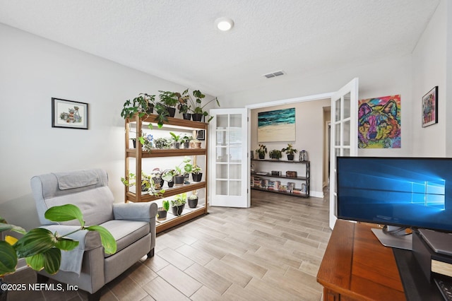 sitting room featuring french doors, a textured ceiling, and light hardwood / wood-style flooring