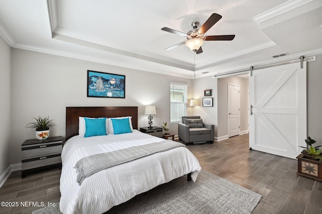 bedroom with ornamental molding, ceiling fan, a tray ceiling, and a barn door