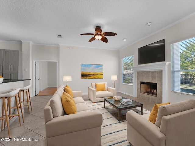 tiled living room featuring a tile fireplace, ornamental molding, a textured ceiling, and ceiling fan