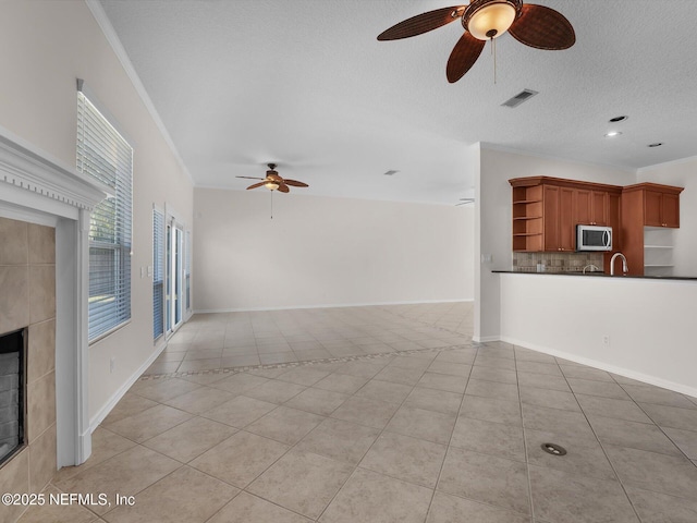 unfurnished living room with light tile patterned floors, crown molding, ceiling fan, a textured ceiling, and a tiled fireplace