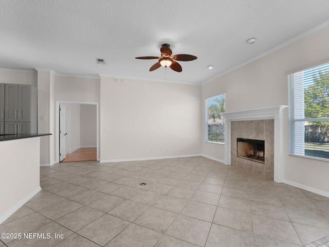 unfurnished living room with a tiled fireplace, crown molding, ceiling fan, and light tile patterned flooring