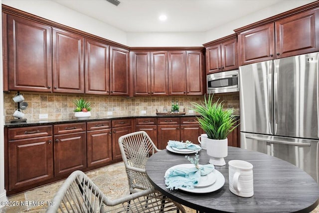 kitchen featuring recessed lighting, appliances with stainless steel finishes, reddish brown cabinets, tasteful backsplash, and dark stone countertops