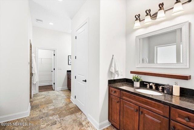 full bathroom with a walk in closet, stone finish floor, vanity, and baseboards