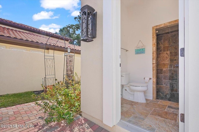 exterior space featuring stone finish floor, baseboards, a shower stall, and toilet