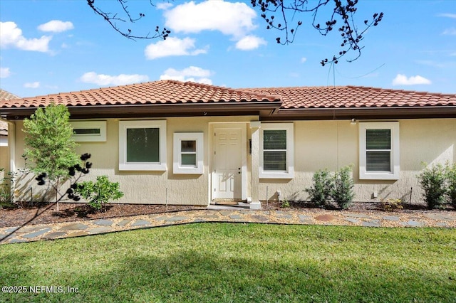 mediterranean / spanish house with a front yard, a tile roof, and stucco siding