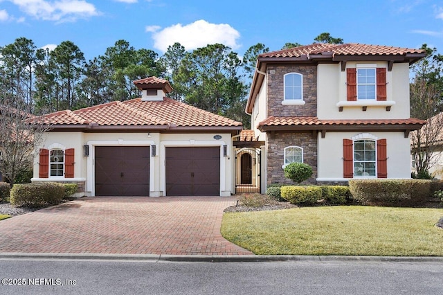 mediterranean / spanish-style home featuring a garage, stone siding, and stucco siding