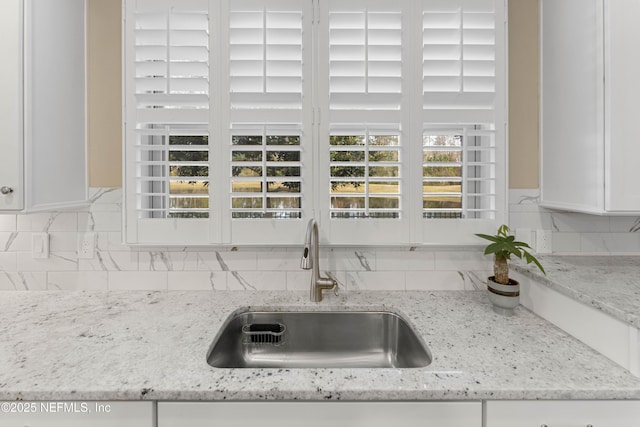 room details with white cabinetry, sink, decorative backsplash, and light stone countertops