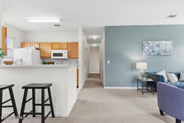 kitchen with white appliances, kitchen peninsula, light carpet, and a breakfast bar area