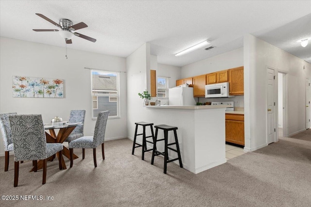 kitchen with white appliances, light carpet, kitchen peninsula, and a textured ceiling