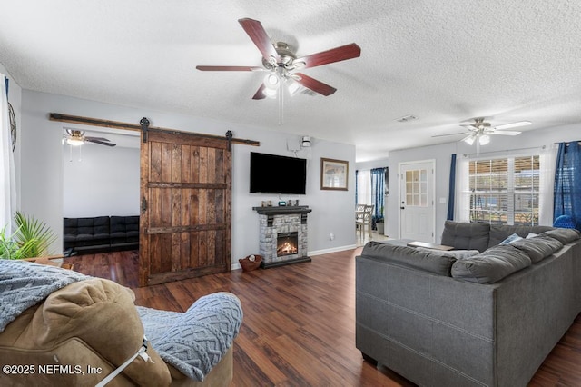 living room featuring a barn door, ceiling fan, dark hardwood / wood-style flooring, a fireplace, and a textured ceiling