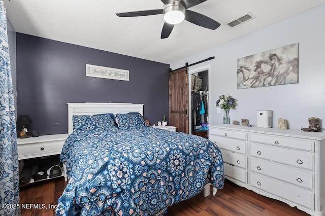 bedroom with ceiling fan, a barn door, a spacious closet, a textured ceiling, and a closet