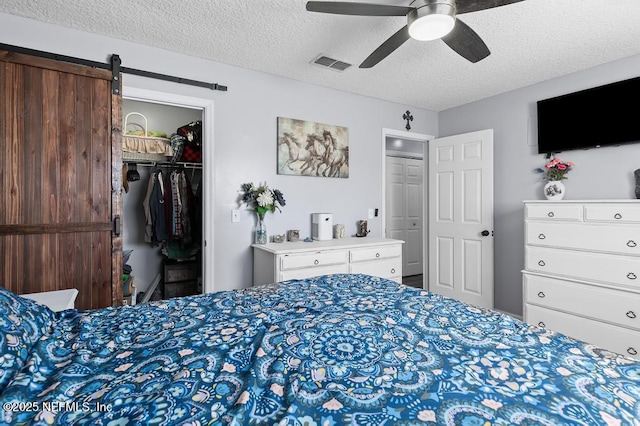 bedroom with ceiling fan, a textured ceiling, and a barn door