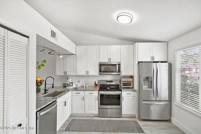 kitchen with lofted ceiling, appliances with stainless steel finishes, white cabinetry, and sink