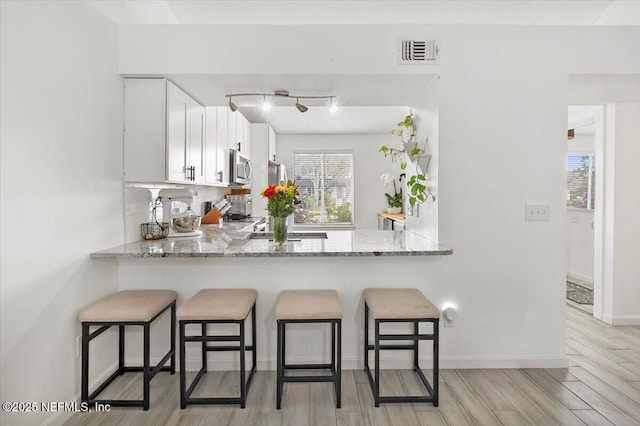 kitchen with white cabinets, light hardwood / wood-style flooring, light stone counters, and kitchen peninsula