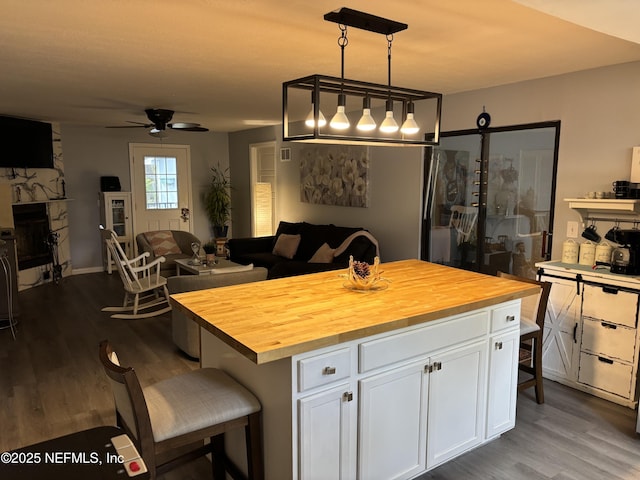 kitchen with butcher block countertops, a kitchen breakfast bar, pendant lighting, white cabinets, and a center island