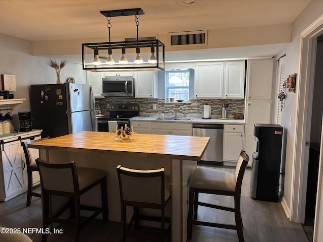 kitchen featuring butcher block counters, stainless steel appliances, decorative backsplash, a kitchen island, and sink