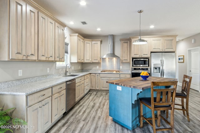 kitchen with wall chimney range hood, a kitchen island, sink, hanging light fixtures, and stainless steel appliances