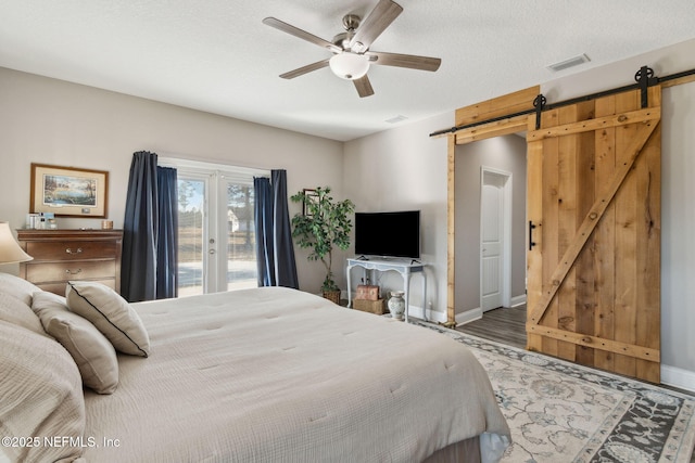 bedroom with ceiling fan, a barn door, access to exterior, wood-type flooring, and a textured ceiling