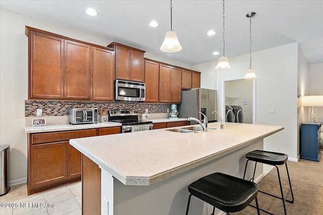 kitchen featuring stainless steel appliances, a breakfast bar, washing machine and clothes dryer, and a kitchen island with sink